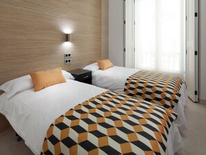 Ein Hotelzimmer mit zwei Betten, einem Holzkopfstück, einem Nachttisch und einem Fenster mit Jalousien.