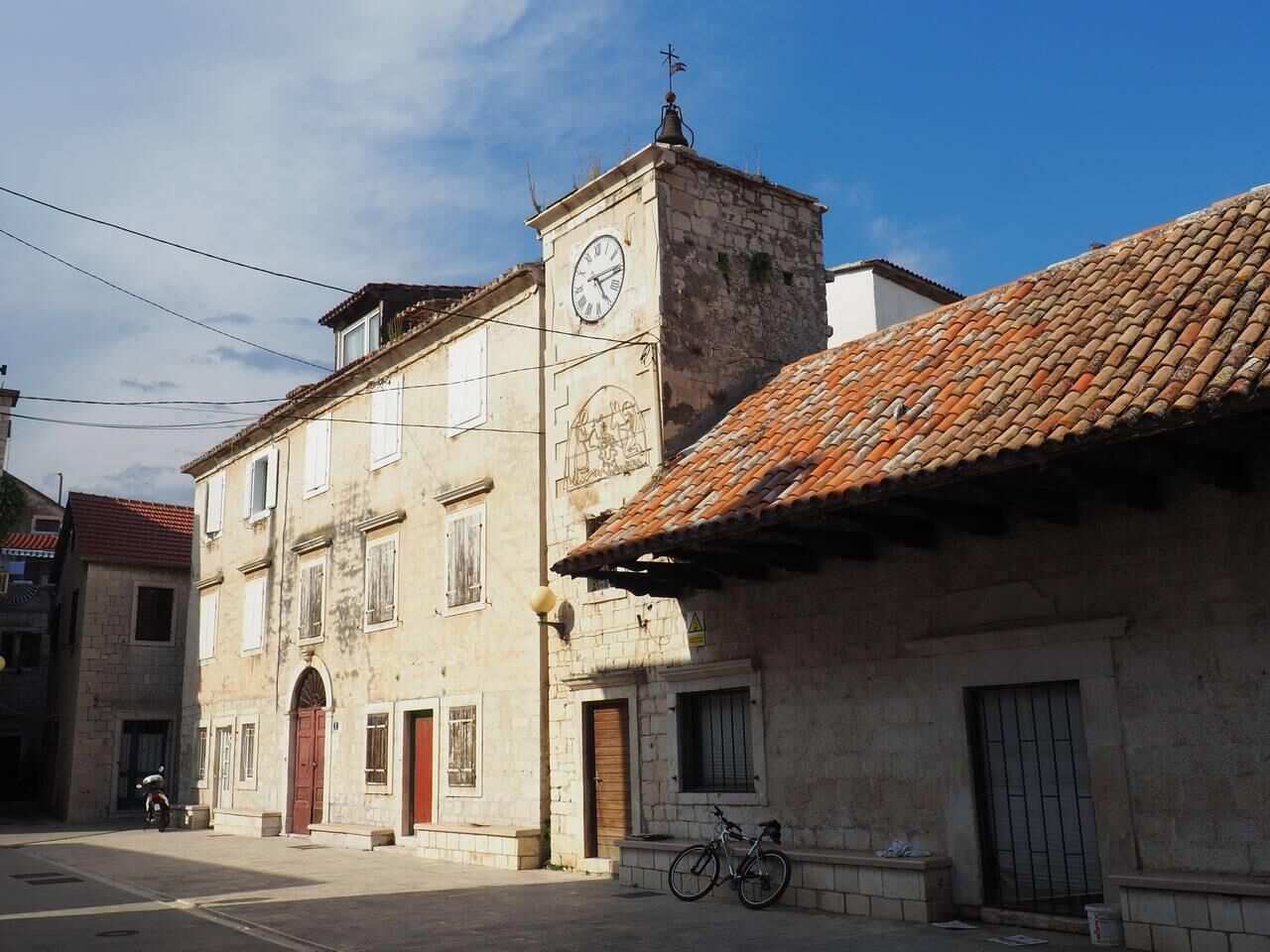A historic building with a clock tower, a red-tiled roof, and a bicycle parked outside.