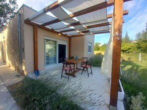 A patio with a table and chairs, a covered area with a pergola, and a sliding glass door to a room.