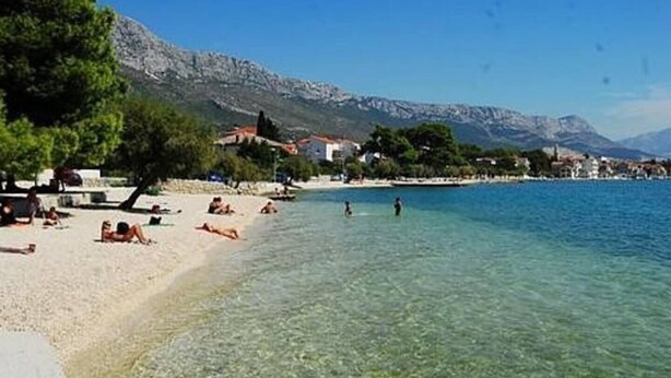 Une plage avec une eau cristalline, des gens qui prennent des bains de soleil et des bâtiments en arrière-plan.