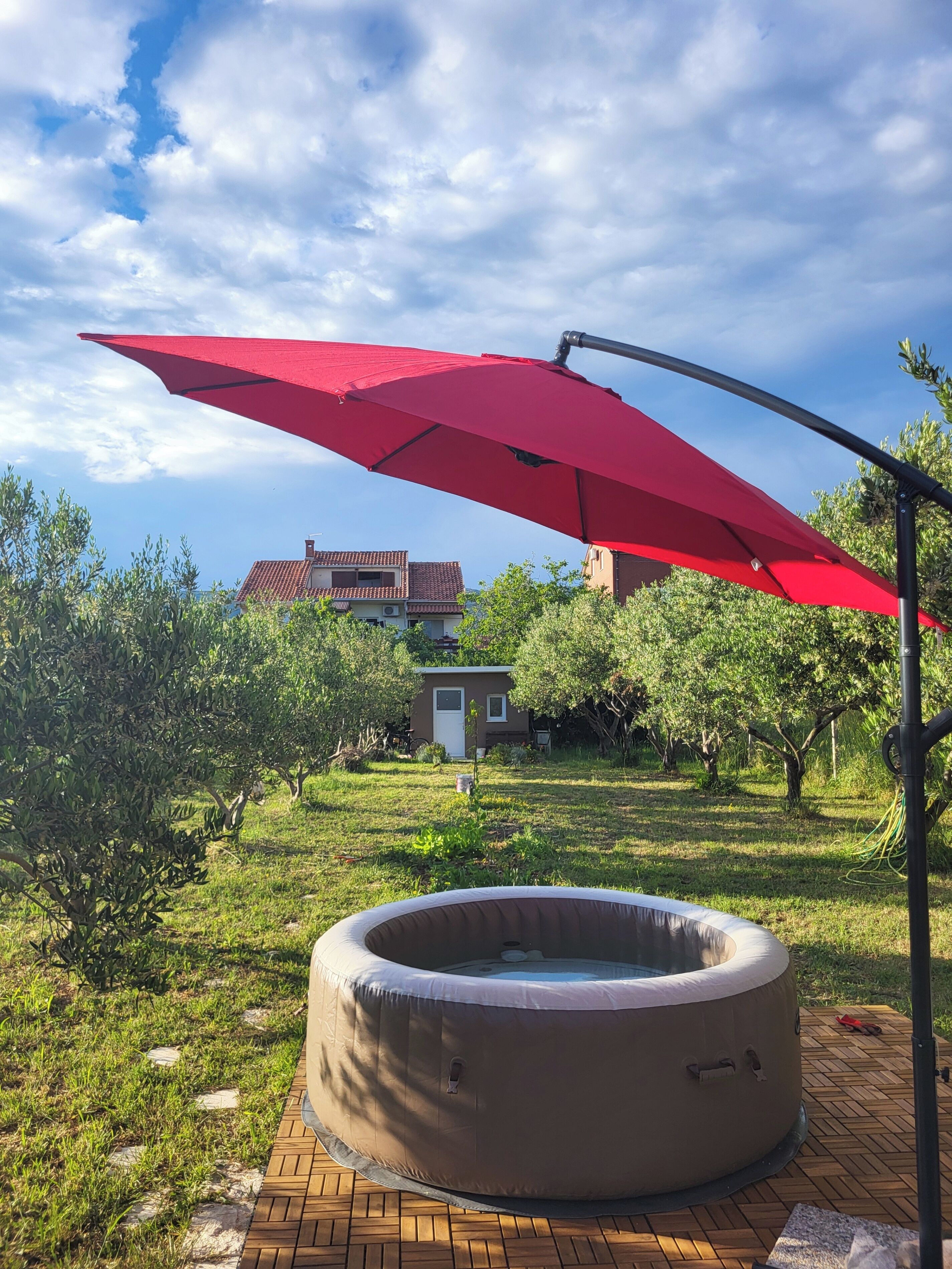 A hot tub on a wooden deck with a red umbrella providing shade.