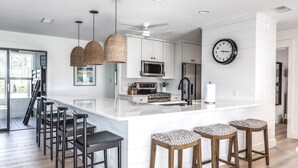 A modern kitchen with a large island, stainless steel appliances, and a clock on the wall.