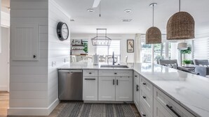 A modern kitchen with white cabinetry, a built-in dishwasher, and a large island with a sink. There are two pendant lights hanging above the island.