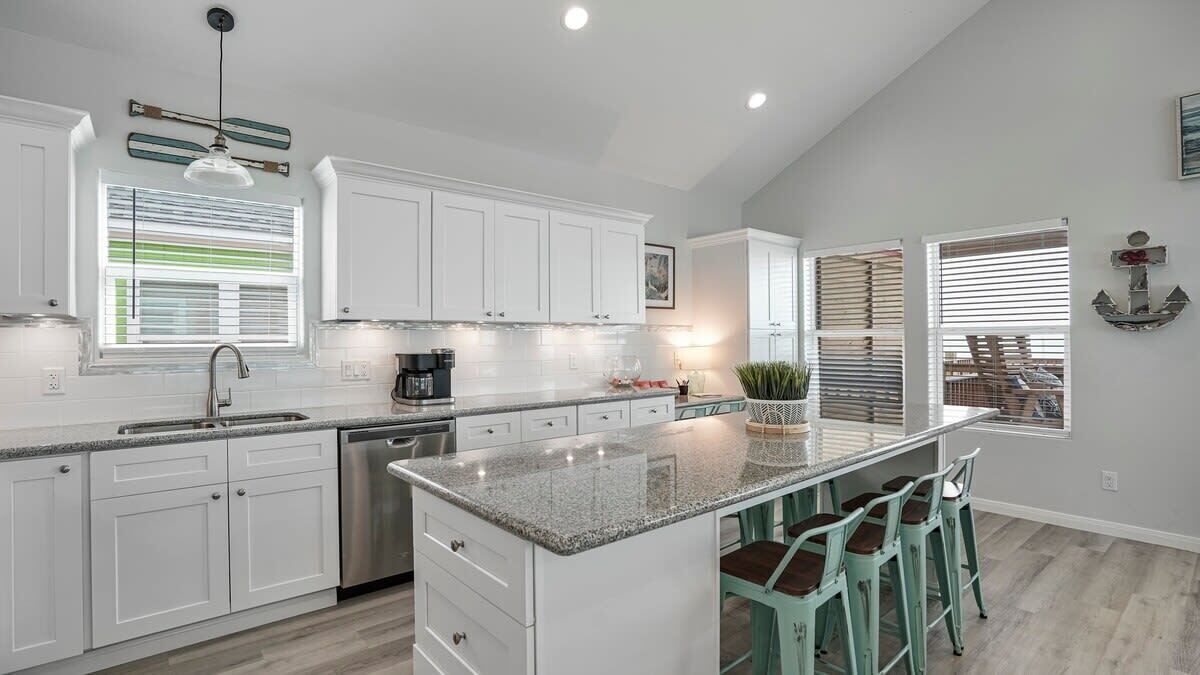 A modern kitchen with white cabinets, a granite countertop, and a central island with bar stools.