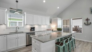 Una cocina moderna con gabinetes blancos, encimera de granito y una isla central con taburetes de bar.