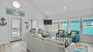 Un salón amplio con un sofá seccional gris grande, sillones turquesa y un televisor de pantalla plana montado en la pared.