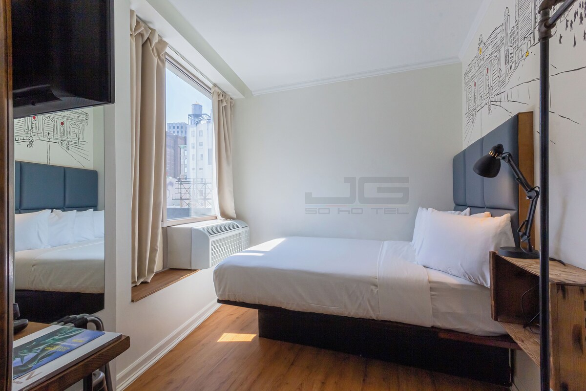 A hotel room with a bed, a desk, a chair, a TV, and a window with curtains.