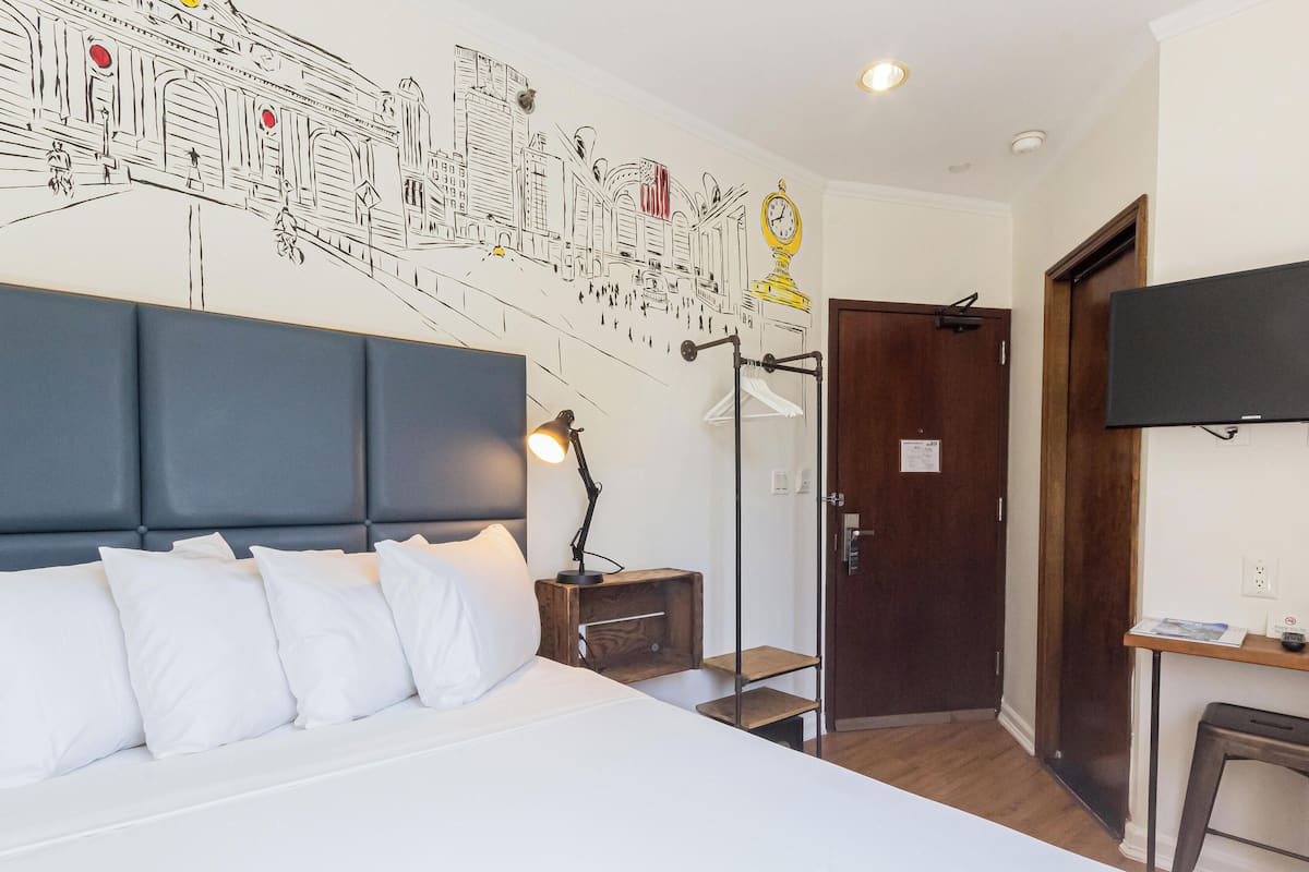 A hotel room with a large bed, a desk with a telephone, a mirror, and a wall with a cityscape mural.