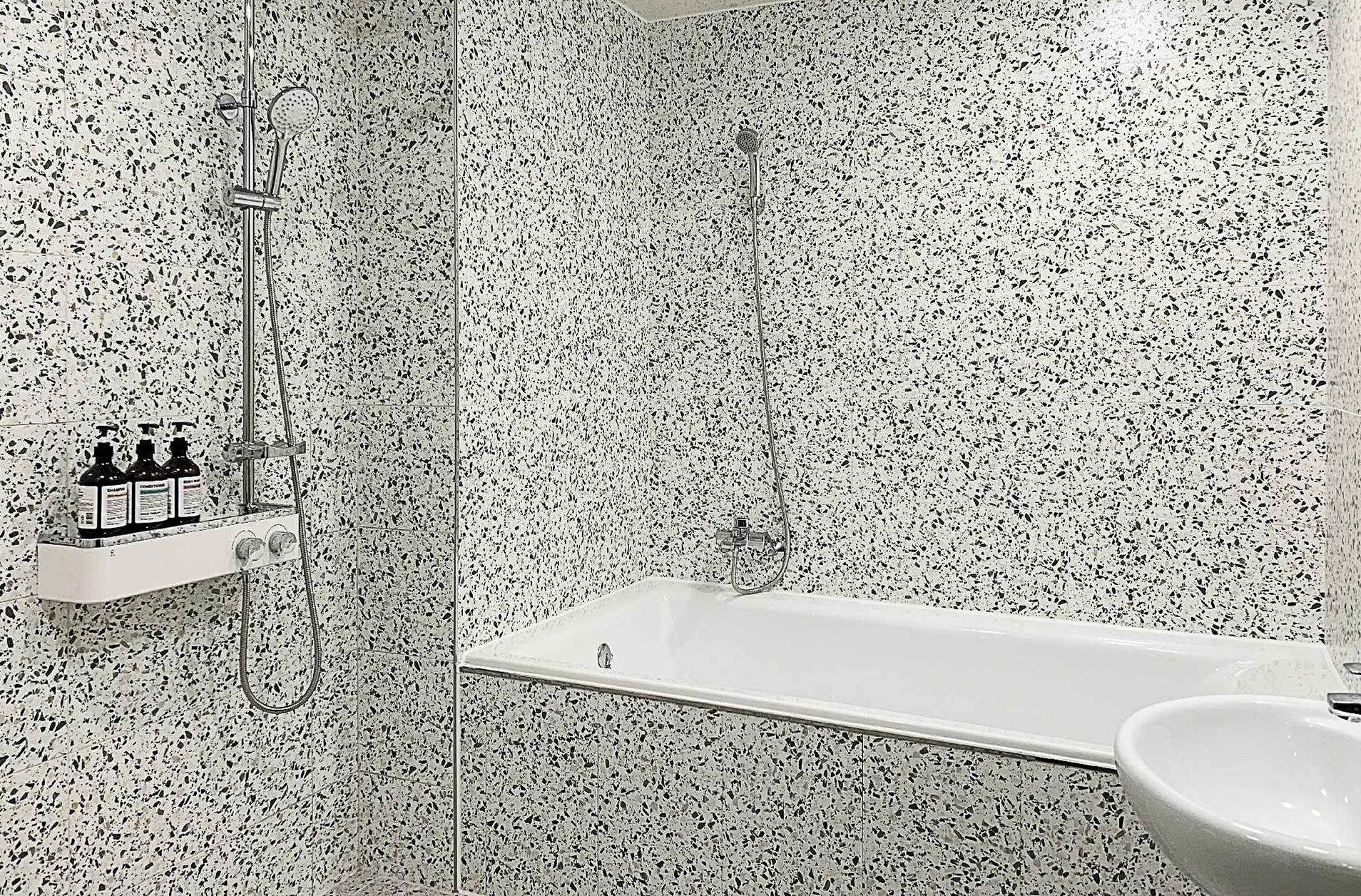 Un baño moderno con una bañera blanca, ducha y lavamanos. Hay tres botellas de champú en un estante.