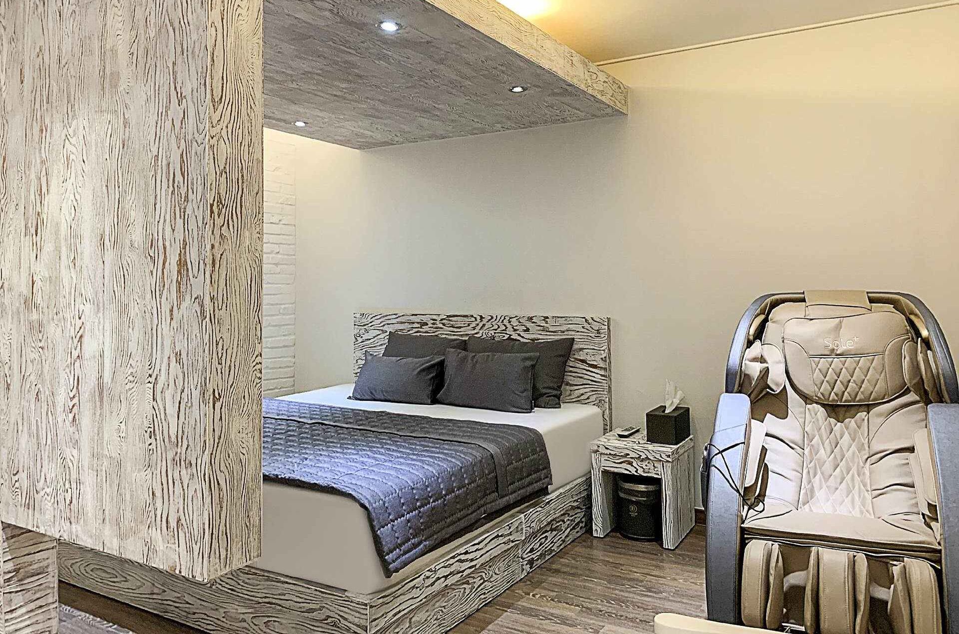 Un dormitorio moderno con cama, sillón de masaje y mesita de noche.