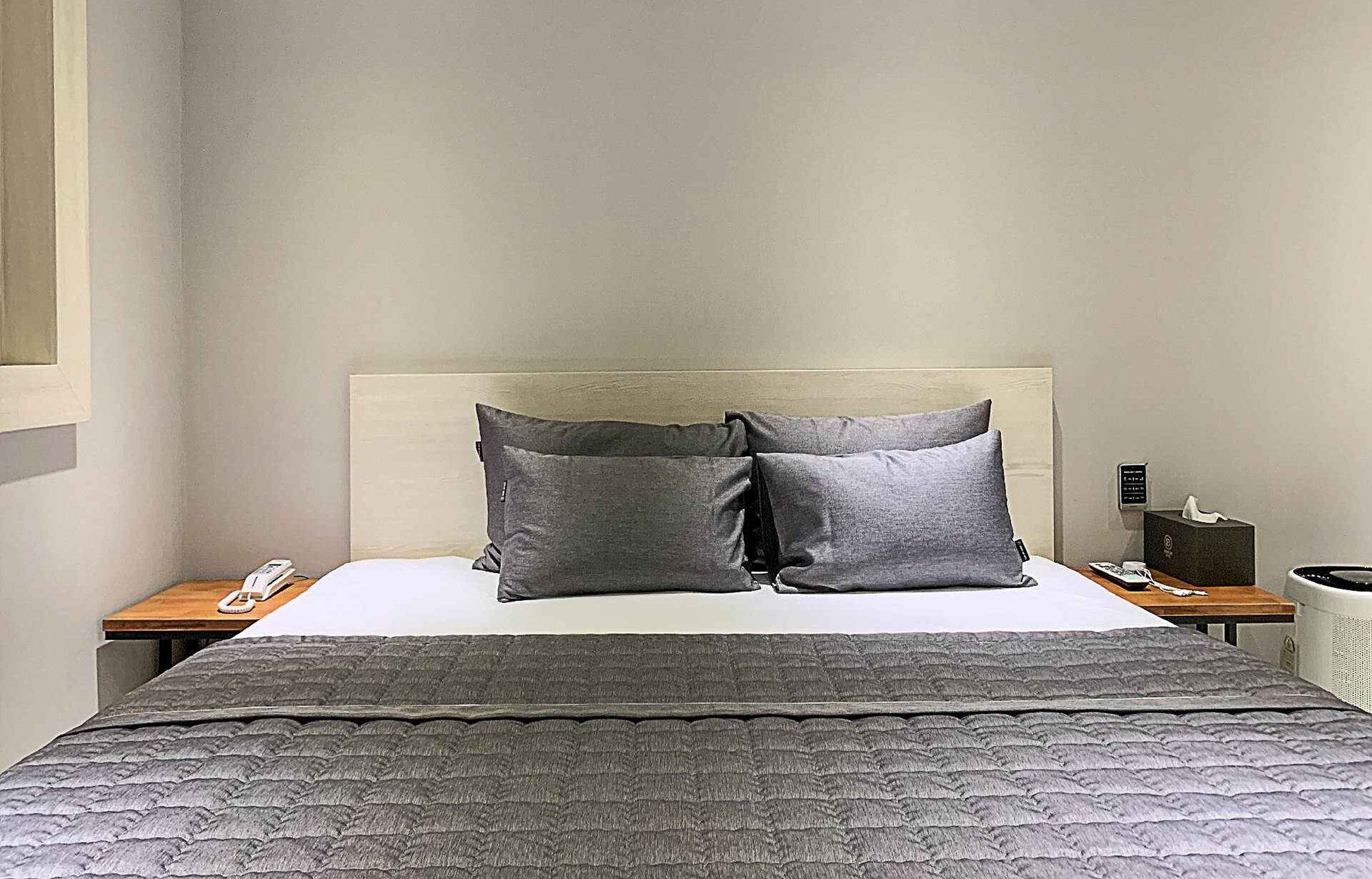 A hotel room with a bed, two pillows, a bedside table with a phone, and a nightstand with a tissue box.