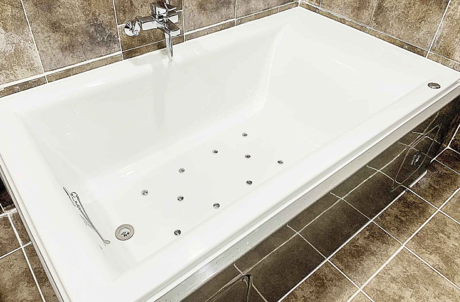 Una bañera blanca con un grifo moderno y varios desagües.