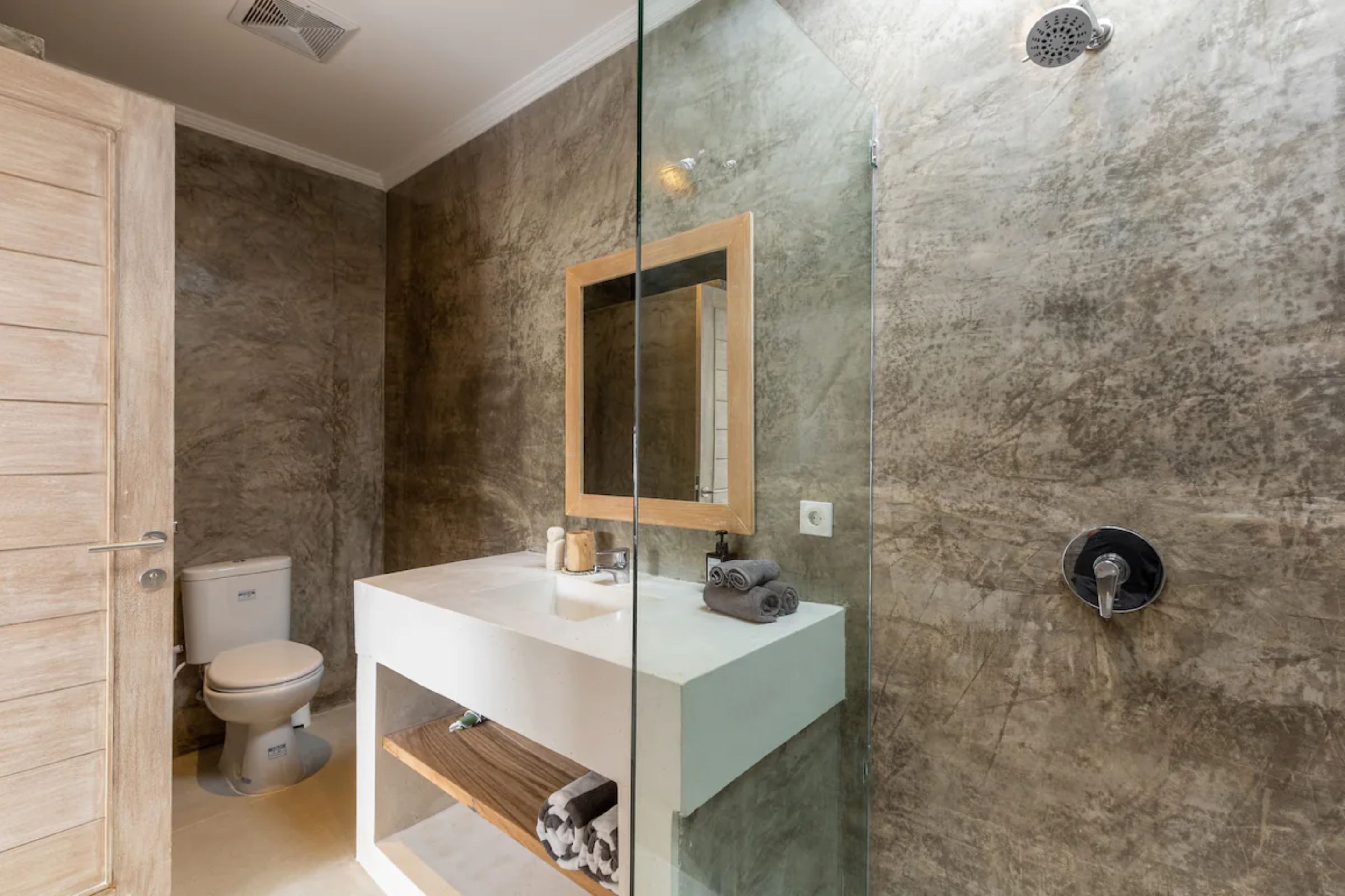 Un baño moderno con cabina de ducha de vidrio, un lavabo blanco y pared de mármol.