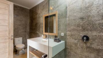 Un baño moderno con cabina de ducha de vidrio, un lavabo blanco y pared de mármol.