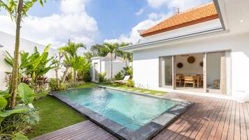 A modern house with a swimming pool, surrounded by lush greenery and a wooden deck.