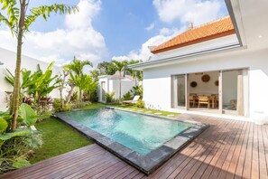 A modern house with a swimming pool, surrounded by lush greenery and a wooden deck. - Villa Casa Cielo by OriVista (Canggu)