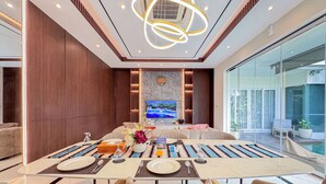 A modern dining area with a large table set for four, a television mounted on the wall, and a view of the outdoors.
