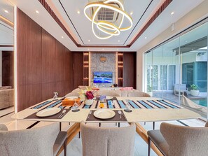 Ein modernes Esszimmer mit einem großen Tisch, gedeckt für vier Personen, einem an der Wand befestigten Fernseher und Blick ins Freie.