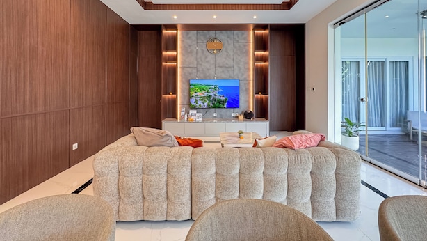 A modern living room with a large flat-screen TV, a sofa, and a glass door leading to an outdoor area.