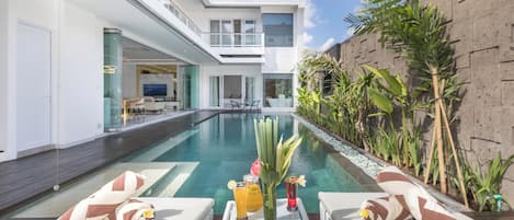 A modern poolside area with lounge chairs, a table with drinks, and a view of the pool.
