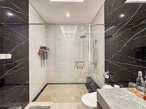 Une salle de bain moderne dotée d’une douche à parois de verre, de toilettes et d’un meuble-lavabo avec un plan de travail en marbre.
