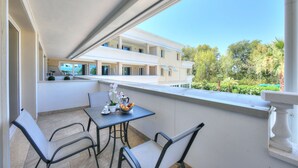 A balcony with a table and chairs, overlooking a building and greenery.