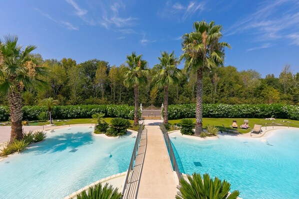 A pool with a central walkway, surrounded by palm trees and greenery.