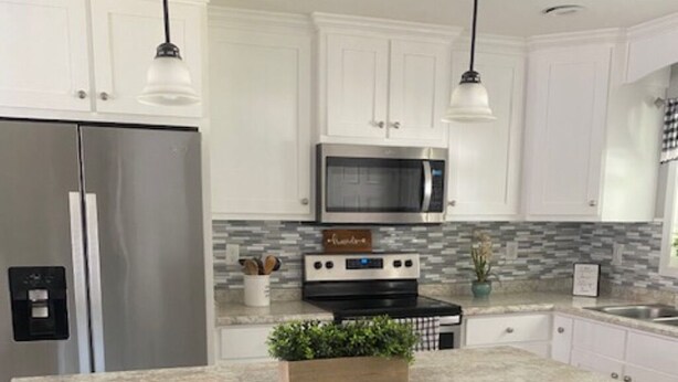 Una cocina con armarios blancos, un refrigerador de acero inoxidable, un microondas y un horno empotrado. Hay tres taburetes de madera con asientos acolchados.
