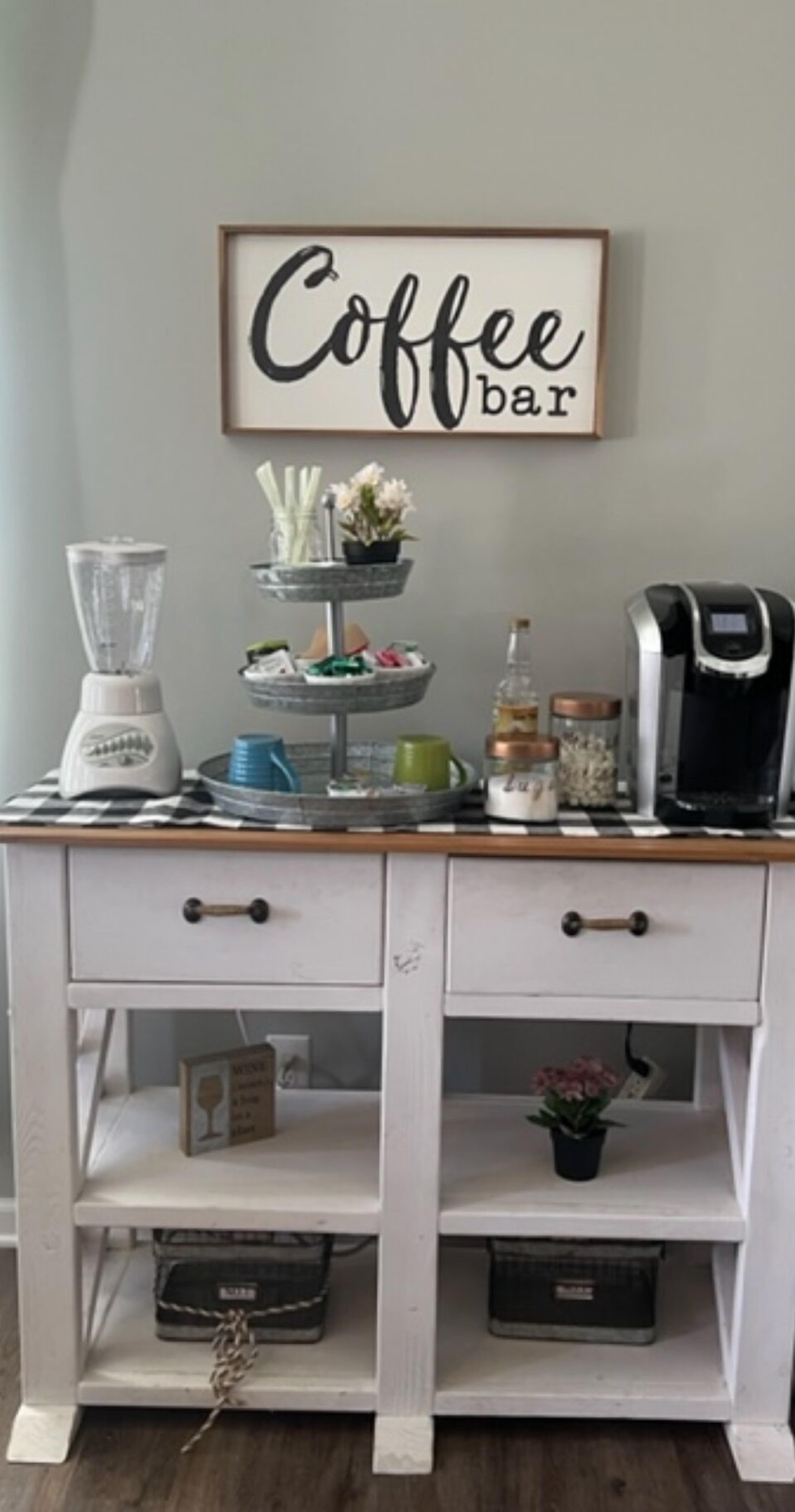 Un piano di lavoro in cucina con un angolo caffè, dotato di frullatore, macchina per il caffè e un vassoio a più livelli con fiori.