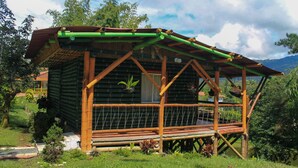 Een houten chalet met een balkon, omgeven door weelderige begroeiing en bomen.