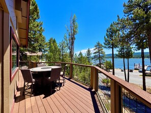 Terraza de madera con mesa y sillas, con vista a un lago con barcos y un muelle.