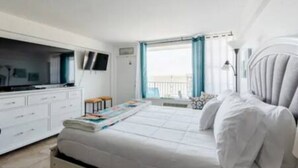 Une chambre à coucher avec un lit, une télévision, un bureau et une fenêtre avec des rideaux.