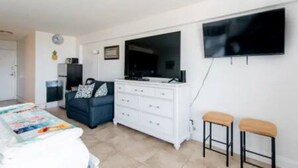 Une chambre à coucher comprenant un lit, une commode, un téléviseur et deux tabourets.