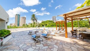Un patio en la azotea con sillones de descanso, una pérgola y vistas de edificios de la ciudad.