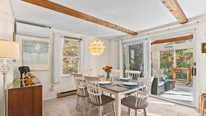 A dining area with a wooden table, white chairs, and a hanging light fixture. - Bike trail, Tennis Court, Surrounded by nature (Eastham)
