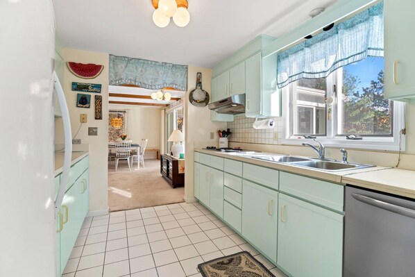 Una cocina con armarios verde claro, un lavamanos de acero inoxidable y una ventana con vistas a árboles.