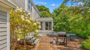 A house with a covered patio, a barbecue grill, and a garden with flowering plants. - Bike trail, Tennis Court, Surrounded by nature (Eastham)