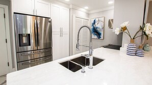 A modern kitchen with stainless steel appliances, a white countertop, and a decorative vase with flowers. - King Suite & Patio | Ground Floor | Monthly Stay | 1BR, Pool, Near Tampa | Saddlebrook Resort (Wesley Chapel)