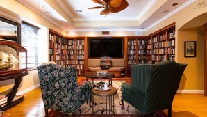 A cozy reading room with a large bookshelf, two armchairs, a round table, and a ceiling fan. - Stylish & Comfy ~ 5★ Location, Office, ♛Queen Bed (Ridgecrest)