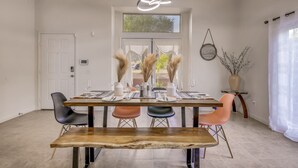 A dining area with a wooden table set for four, surrounded by modern chairs, a bench, and a decorative ceiling light. - House Rising ☀️ Villa w/ mini-golf, pool and spa (Desert Hot Springs)