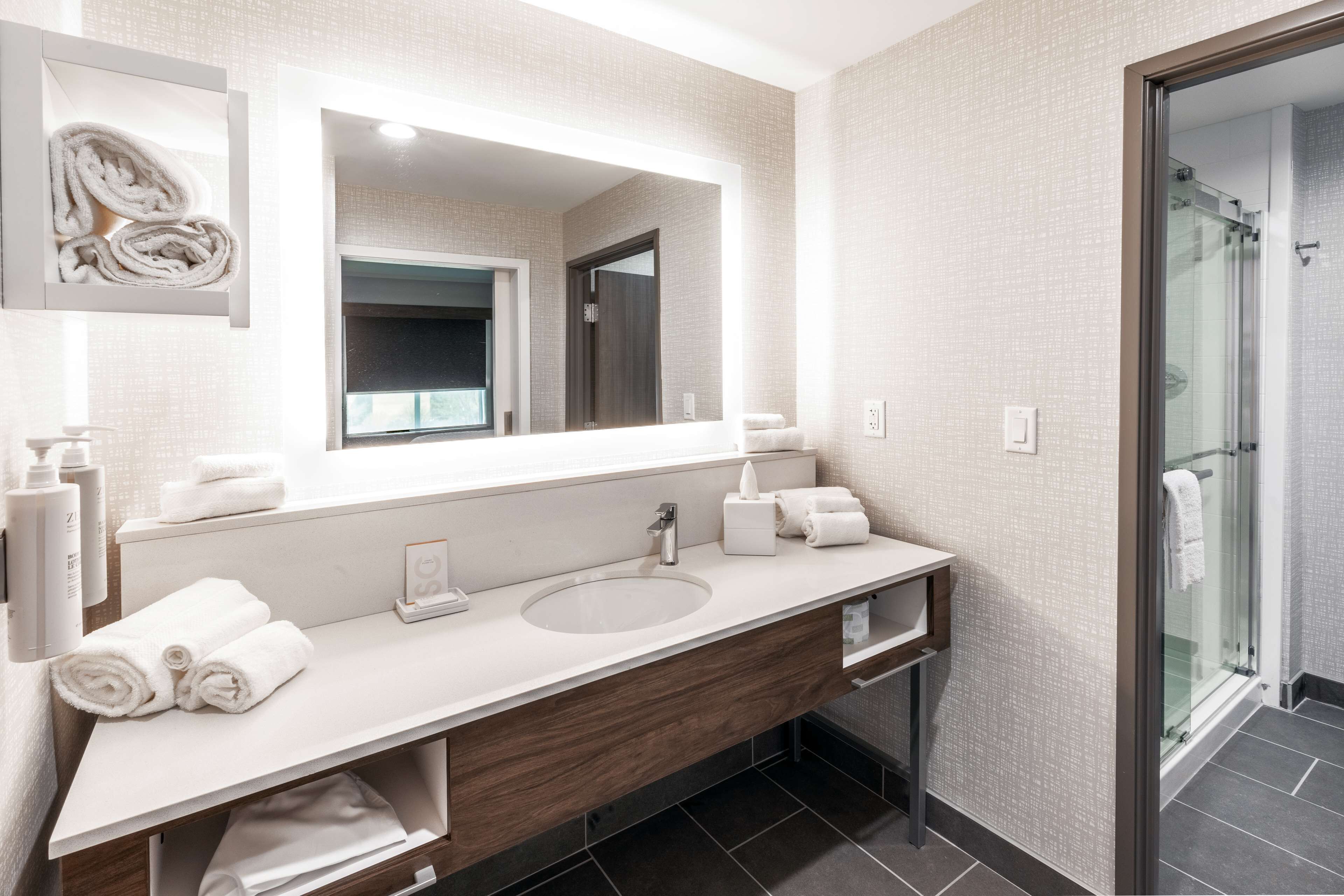 A modern bathroom with a large mirror, a sink, and a shower area.