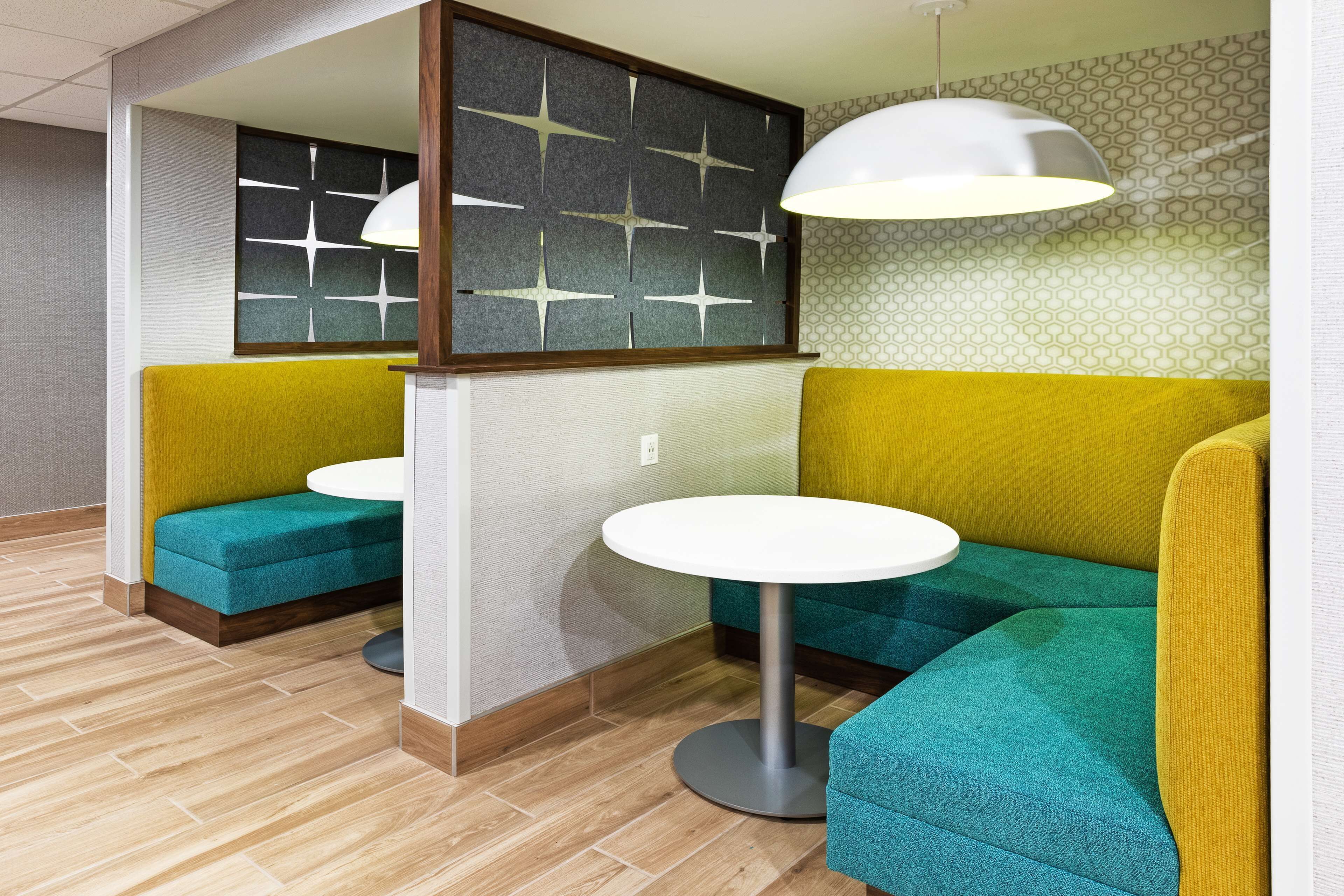 Un intérieur moderne avec des sièges aux couleurs turquoise et moutarde, une table ronde blanche et un mur orné d’un motif géométrique.