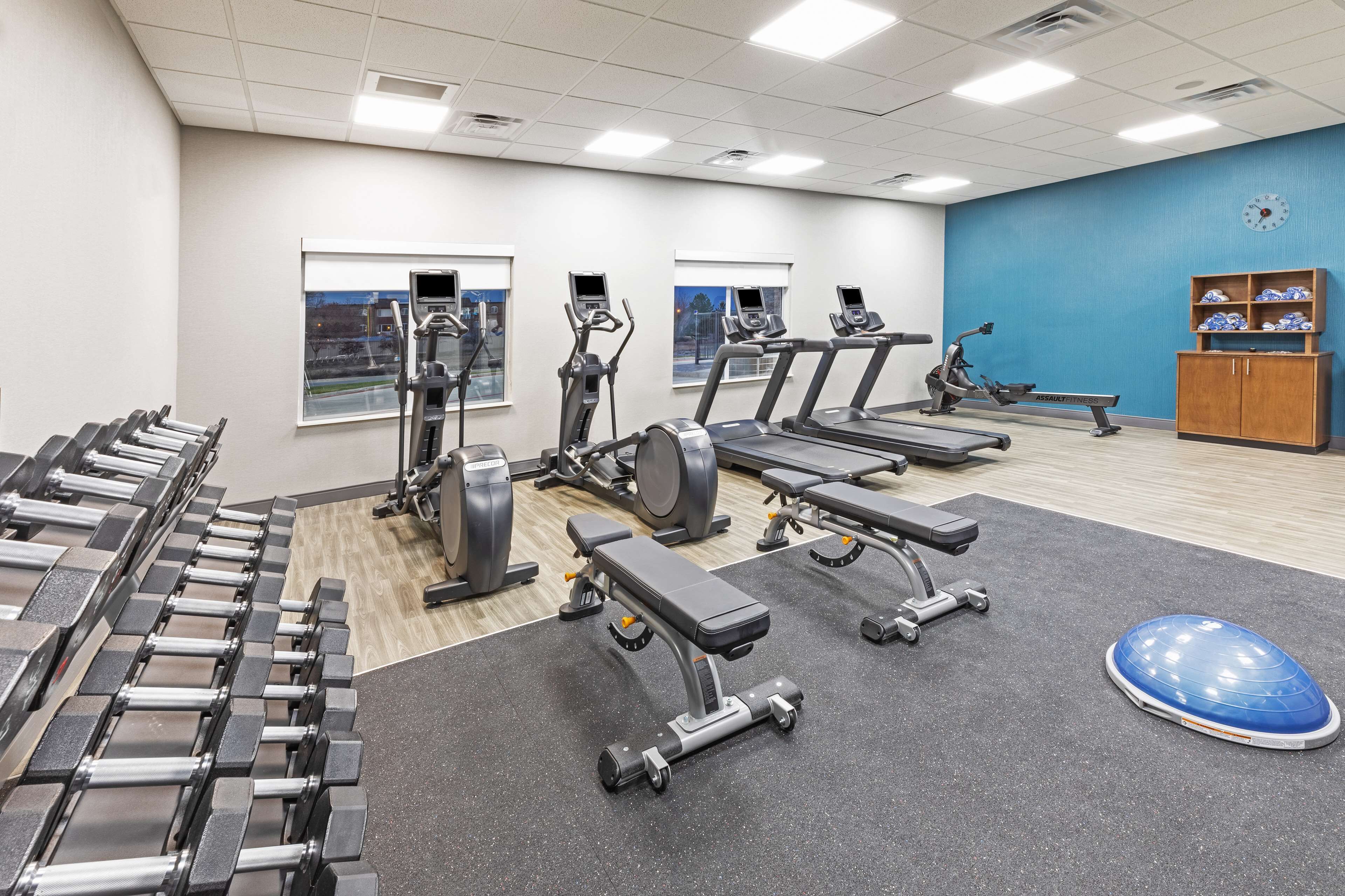 Una palestra con tapis roulant, macchinari ellittici, manubri e una palla da ginnastica blu.