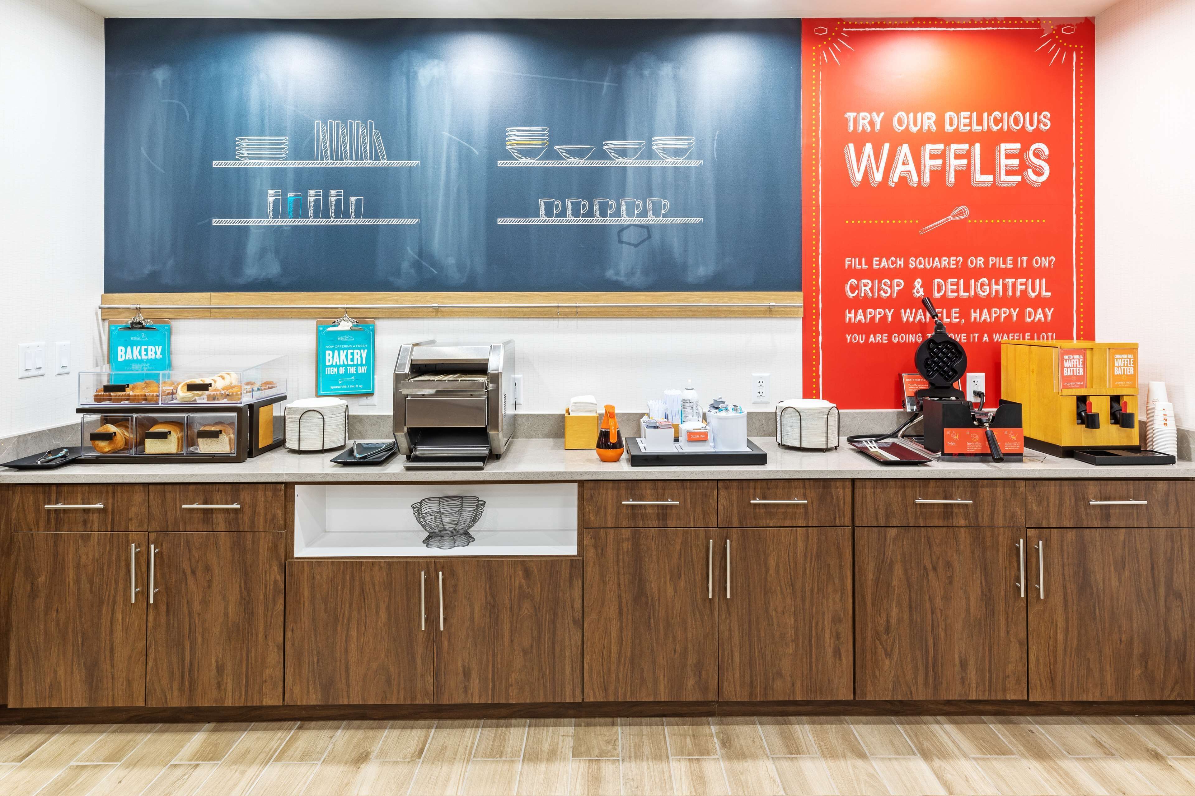 A bakery counter with waffle-making equipment, a chalkboard with waffle designs, and a red promotional sign for waffles.