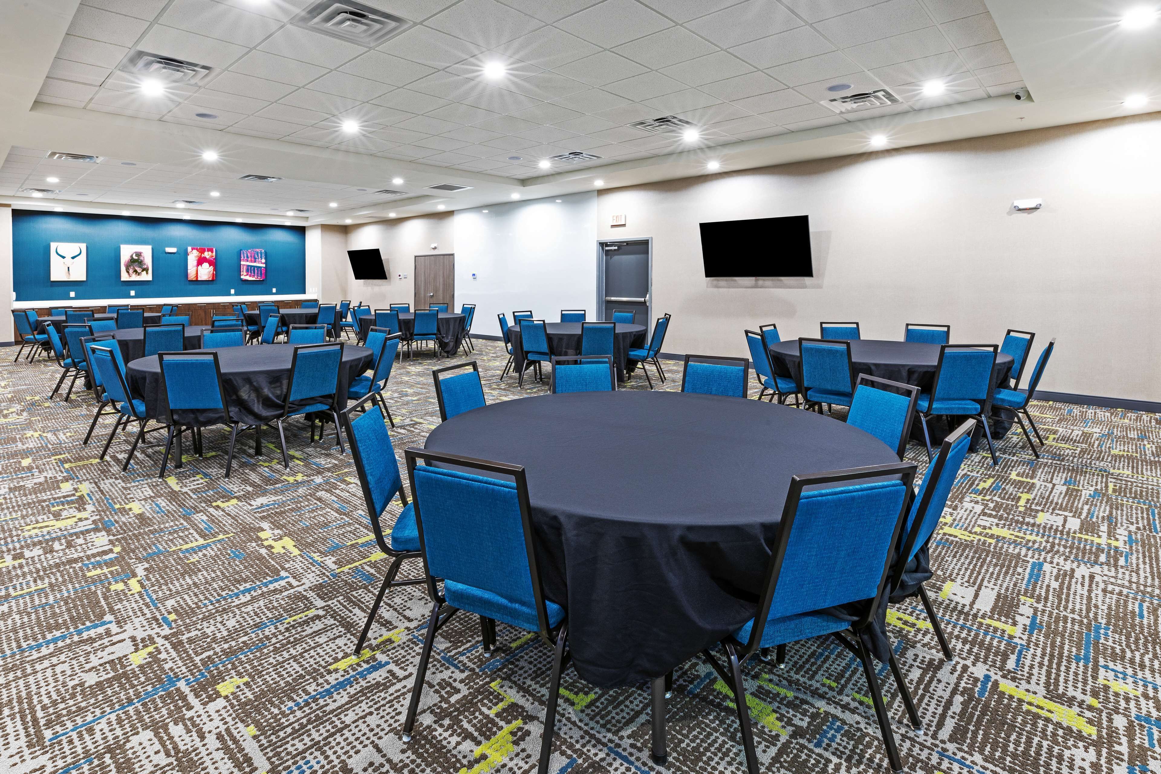 A conference room with multiple tables and chairs, a patterned carpet, and a blue accent wall with artwork.