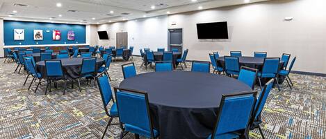 A conference room with multiple tables and chairs, a patterned carpet, and a blue accent wall with artwork.