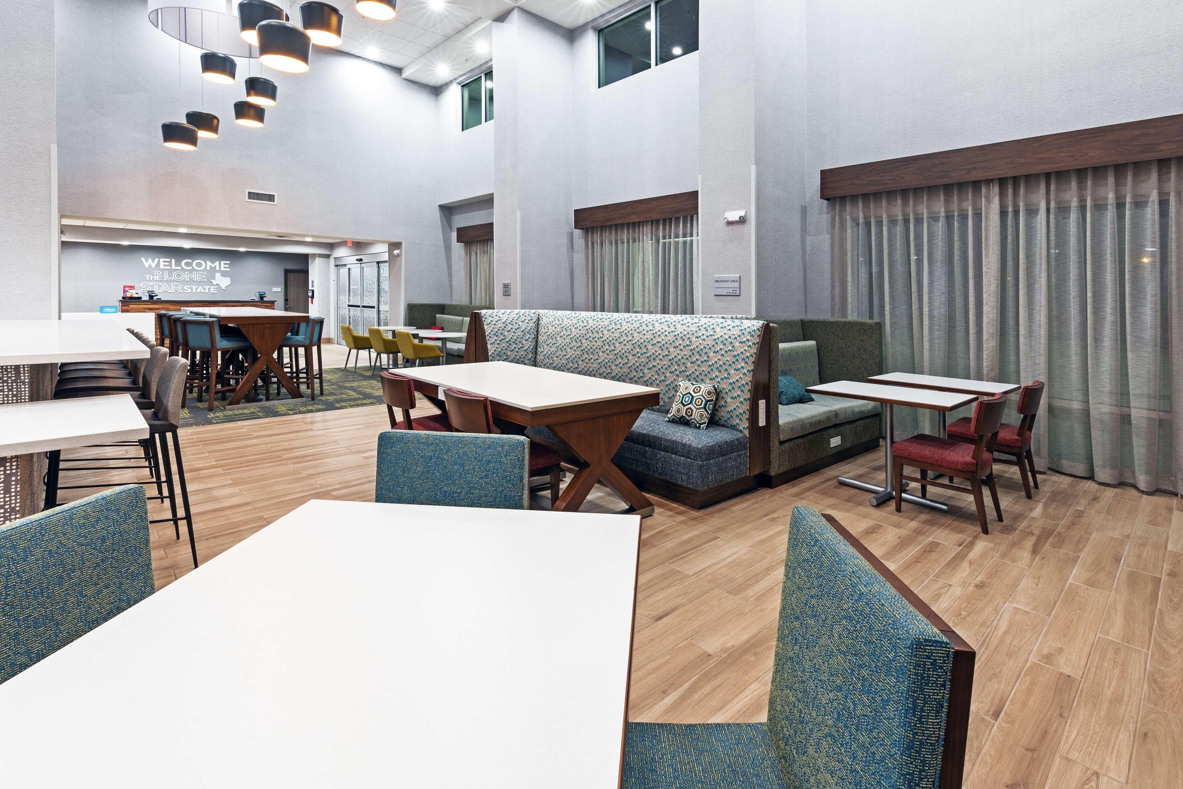A modern hotel lobby with a reception desk, seating areas, and a large window with curtains.