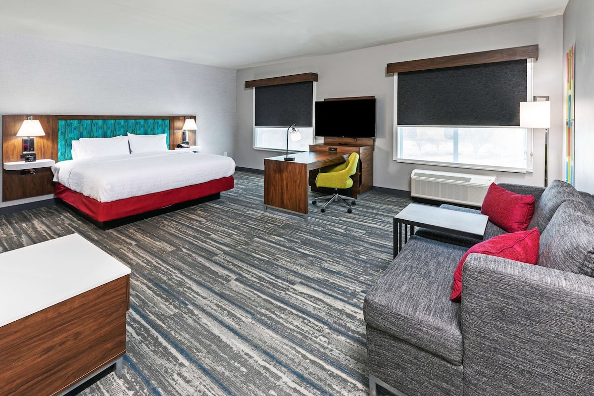 A hotel room with a bed, a desk with a chair, a sofa, and a TV.