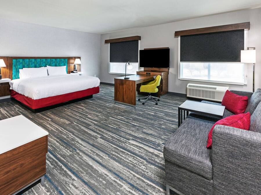 A hotel room with a bed, a desk with a chair, a sofa, and a TV.