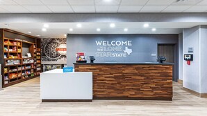 A hotel reception area with a wooden reception desk, a wall sign reading "WELCOME TO THE LONE STAR STATE," and a self-service kiosk. - Hampton Inn & Suites Canyon (Canyon)